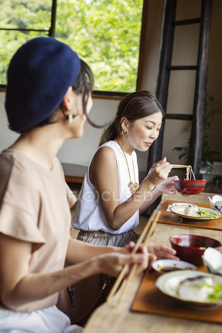 Dos mujeres japonesas sentadas en una mesa en un restaurante japonés, comiendo . - foto de stock