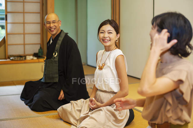 Two Japanese women and Buddhist priest kneeling in Buddhist temple, talking. — Stock Photo