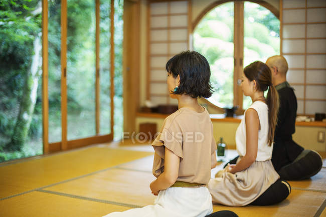 Two Japanese women and Buddhist priest kneeling in Buddhist temple, praying. — Stock Photo
