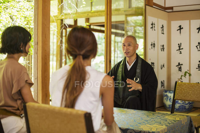 Zwei Frauen und ein buddhistischer Priester knien im buddhistischen Tempel und reden. — Stockfoto
