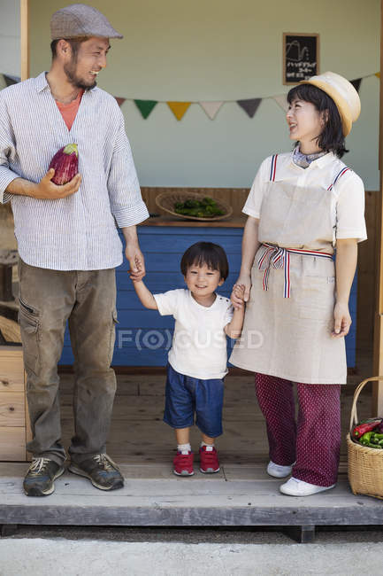 Giapponese uomo, donna e ragazzo in piedi al di fuori di un negozio di fattoria, tenendosi per mano . — Foto stock