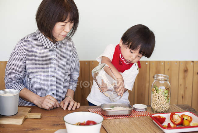 Mature Japanese woman and boy standing in a farm shop, preparing food. — Stock Photo