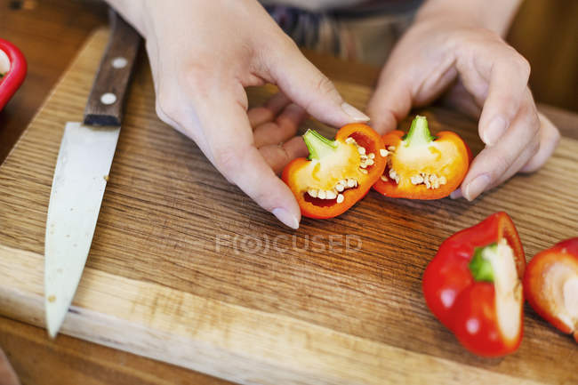 Alto ângulo close-up de pessoa que corta pimentas vermelhas frescas na placa de corte de madeira . — Fotografia de Stock