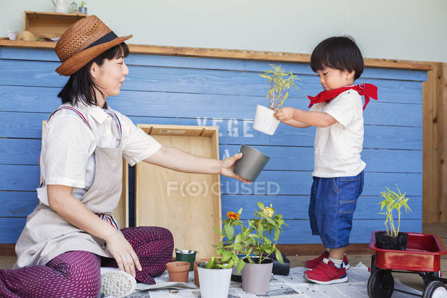 Mulher japonesa vestindo chapéu e menino sentado fora de uma loja de fazenda, plantando flores em vasos de flores . — Fotografia de Stock