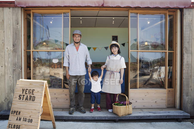 Giapponese uomo, donna e ragazzo in piedi al di fuori di una fattoria negozio, tenendosi per mano, guardando in macchina fotografica . — Foto stock