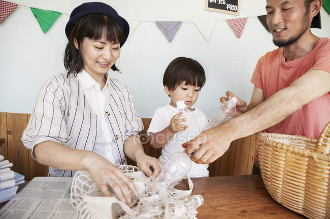 Japanese man, woman and boy standing in a farm shop, sorting clear plastic bottles into basket. — Stock Photo
