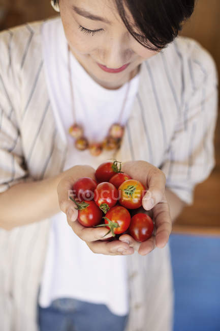 High angle close-up of Japanese woman holding fresh tomatoes. — Stock Photo
