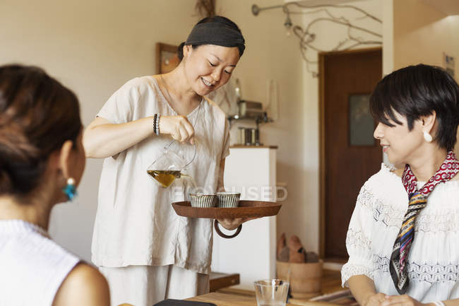 Japanese woman serving tea to female customers in a vegetarian cafe. — Stock Photo