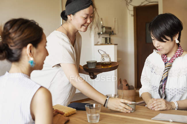 Japanese woman serving tea to female customers in a vegetarian cafe. — Stock Photo