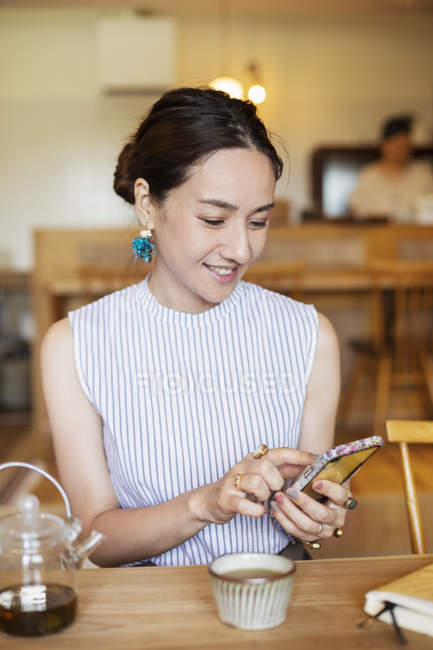 Японка сидит за столом в вегетарианском кафе, используя мобильный телефон . — стоковое фото
