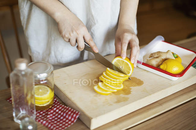 High angle close-up of person cutting lemon slices with knife on wooden cutting board. — Stock Photo