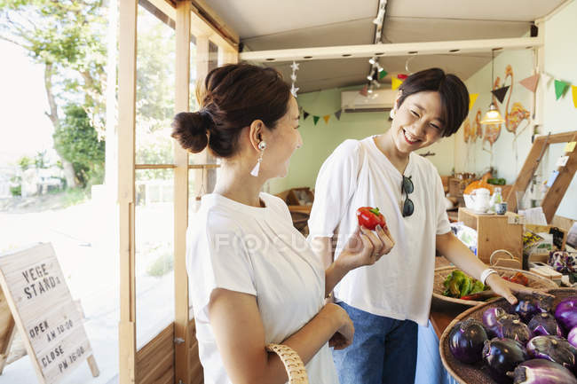 Дві усміхнені японські жінки дивляться на свіжі овочі в фермерському магазині.. — стокове фото