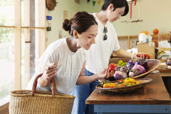 Two smiling Japanese women looking at fresh vegetables in a farm shop. — Stock Photo