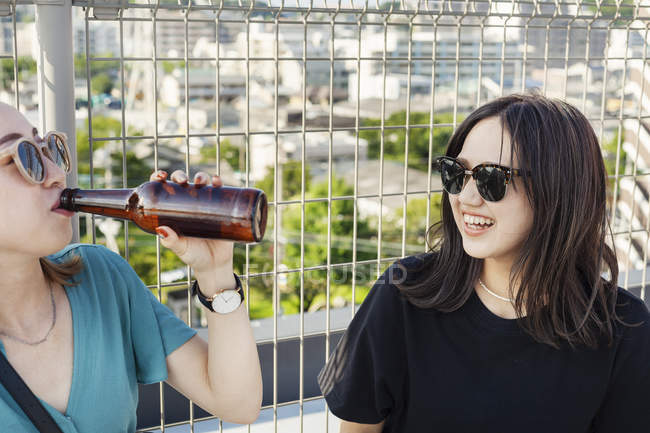 Дві молоді жінки з Японії сидять на даху в місті і п 
