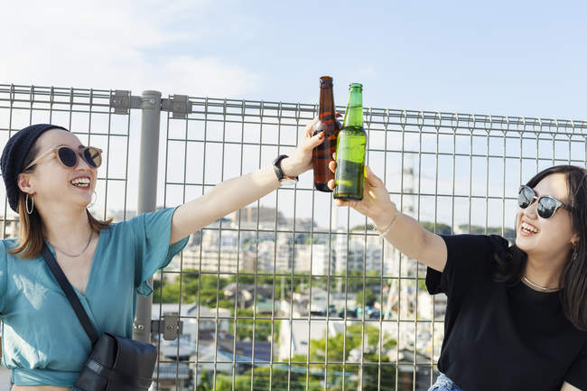 Jeunes Japonaises assises sur le toit en milieu urbain, grillant de la bière
. — Photo de stock