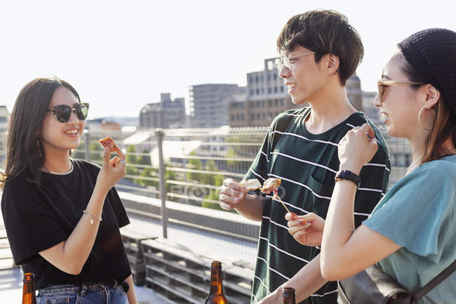 Jovem japonês homem e mulheres de pé no telhado em ambiente urbano, comer lanches . — Fotografia de Stock