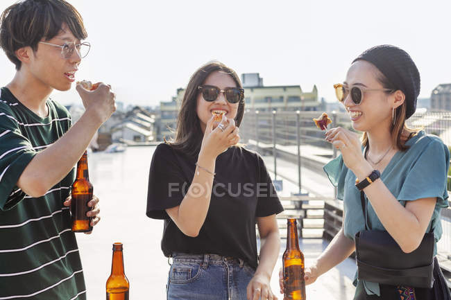 Young Japanese man and women standing on rooftop in urban setting, eating snacks. — Stock Photo