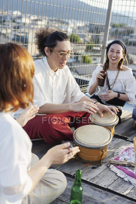 Japanische Frauen und Männer sitzen auf einem Dach in urbaner Umgebung und spielen Schlagzeug. — Stockfoto