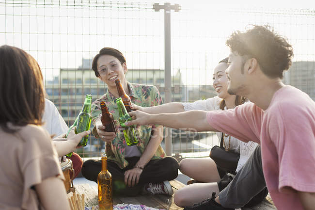 Gruppe junger japanischer Männer und Frauen sitzt auf einem Dach in urbaner Umgebung und trinkt Bier. — Stockfoto