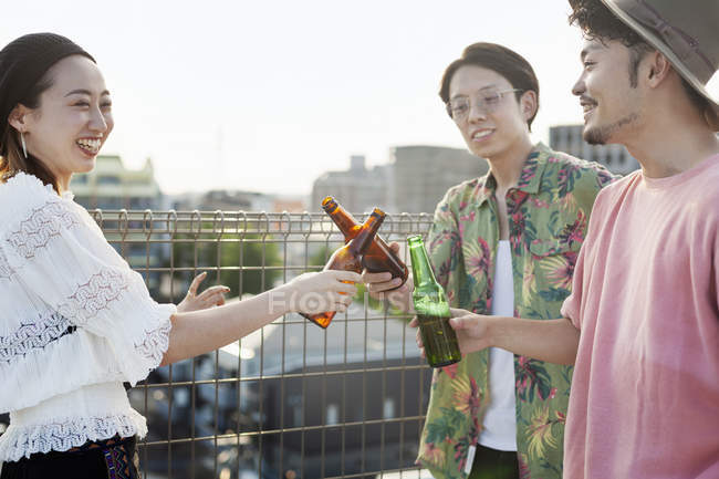 Young Japanese men and woman standing on rooftop in urban setting, drinking beer. — Stock Photo