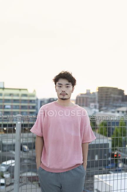 Молодий японець стоїть на даху в місті і дивиться в камеру.. — стокове фото