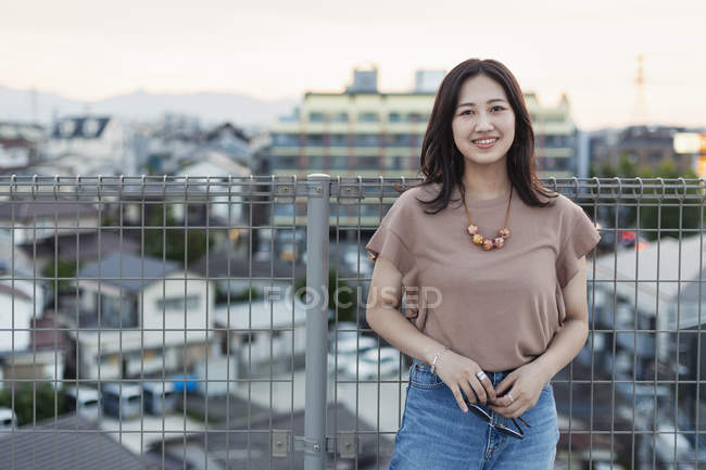 Young Japanese woman standing on rooftop in urban setting, looking in camera. — Stock Photo