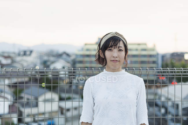 Young Japanese woman standing on rooftop in urban setting, looking in camera. — Stock Photo