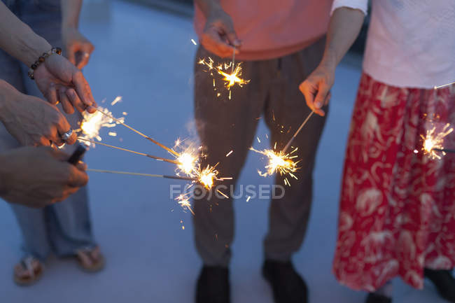 Hands of men and women with sparklers on rooftop. — Stock Photo