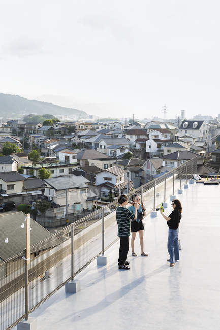 Vista de ángulo alto de hombres y mujeres jóvenes japoneses que beben cerveza en la azotea en un entorno urbano . - foto de stock