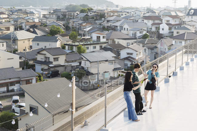 Vista de ángulo alto de hombres y mujeres jóvenes japoneses que beben cerveza en la azotea en un entorno urbano . - foto de stock