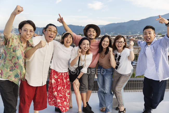 Sonriente grupo de jóvenes japoneses hombres y mujeres de pie en la azotea en el entorno urbano
. - foto de stock