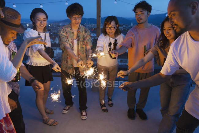 Group of young Japanese men and women with sparklers on rooftop in urban setting. — Stock Photo