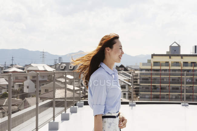 Lächelnde Japanerin steht auf einem Dach in urbaner Umgebung. — Stockfoto