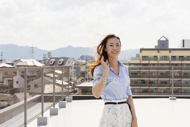 Junge Japanerin steht auf einem Dach in urbaner Umgebung und blickt in die Kamera. — Stockfoto