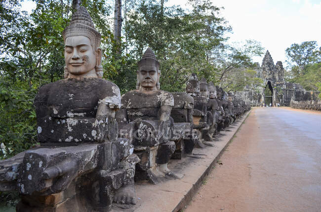 Angkor Wat, a 12th century historic Khmer temple and UNESCO world heritage site. Busts and statues of deities and guardian figures along a path to a stupa and entrance arch. — Stock Photo