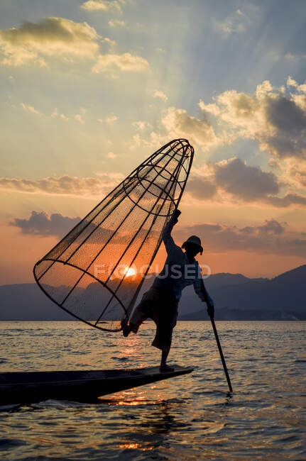 Tradizionale pescatore bilanciamento su una gamba su una barca, in possesso di cesto di pesca, pesca sul lago Inle al tramonto, Myanmar. — Foto stock