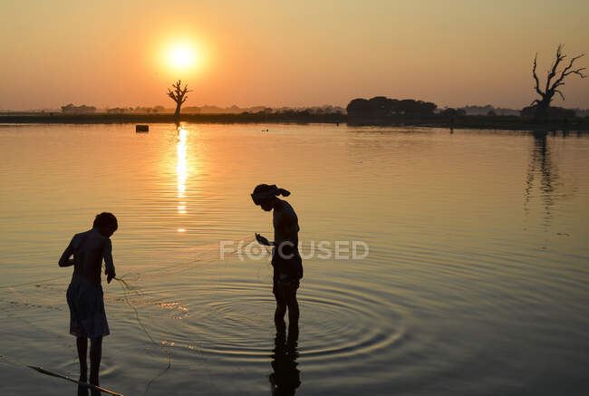 Два мальчика ловят рыбу в озере на закате, Амапура, Мьянма. — стоковое фото