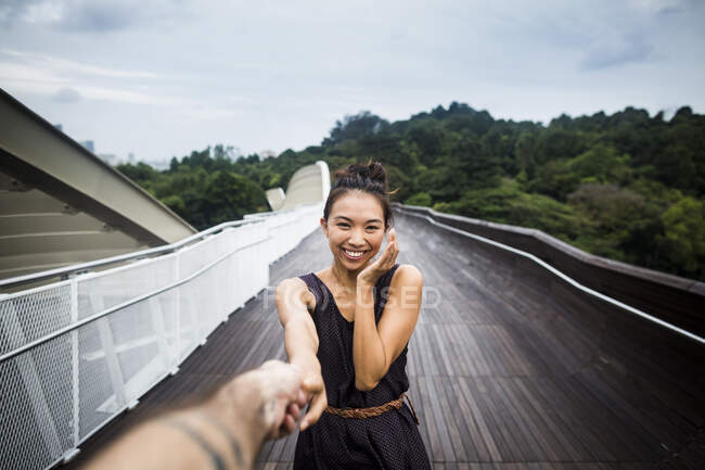 Sorrindo jovem de pé em uma ponte, segurando mão masculina. — Fotografia de Stock