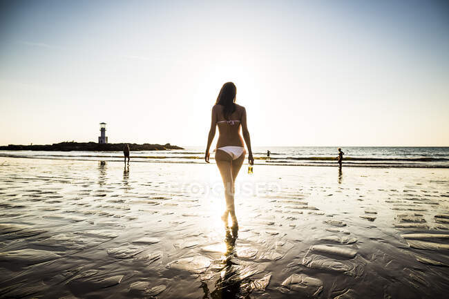 Visão traseira da mulher caminhando em direção à praia durante o pôr do sol. — Fotografia de Stock