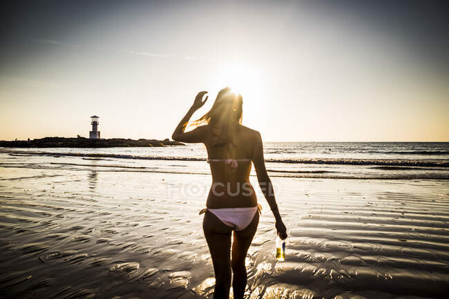Visão traseira da mulher caminhando em direção à praia durante o pôr do sol. — Fotografia de Stock