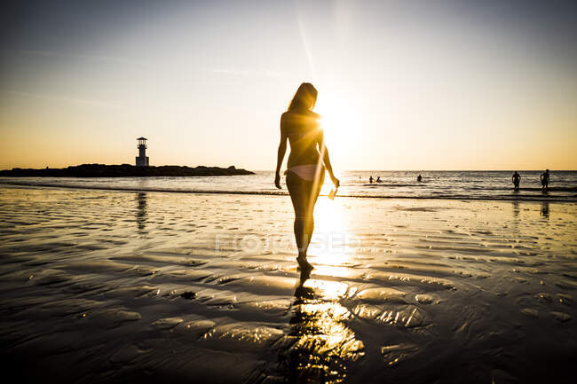 Vue arrière d'une femme marchant vers la plage au coucher du soleil. — Photo de stock
