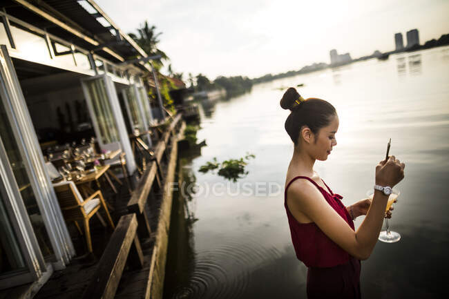 Woman drinking ginger-lemongrass martini at a bar on the bank of a river. — Stock Photo