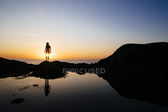 Силует жінки, що стоїть на скелі біля океану на заході сонця . — стокове фото