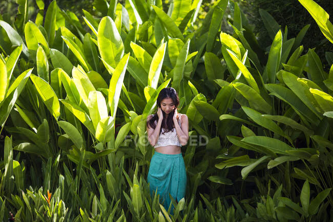 Молодая женщина, стоящая в тропическом лесу с пышной зеленой листвой. — стоковое фото