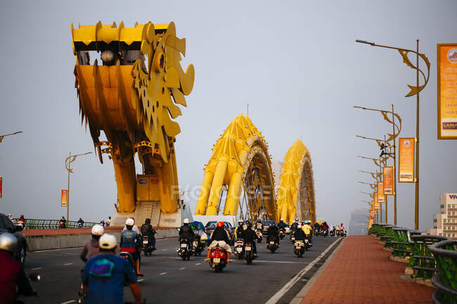 Rückansicht von Pendlern auf Motorrädern, die eine Brücke in Form eines Drachen überqueren. — Stockfoto