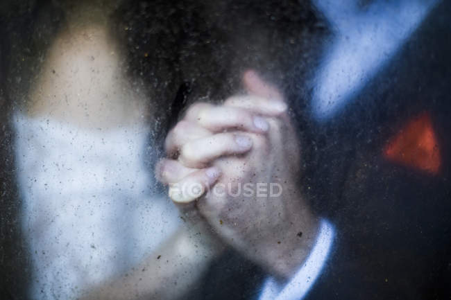 Крупним планом через брудне вікно пари, що тримає руки . — стокове фото