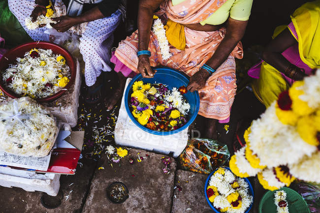 Primer plano de alto ángulo de las mujeres que atan flores en cuerdas en el mercado en la India . - foto de stock