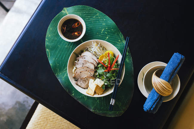 Primo piano ad angolo alto di ciotola di tagliatelle Cao Lau con carne di maiale alla griglia ed erbe aromatiche . — Foto stock