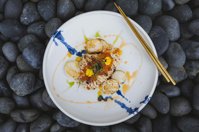 High angle close-up of scallop somen with fish roe, ebi and salted egg yolk sauce on black stones. — Stock Photo