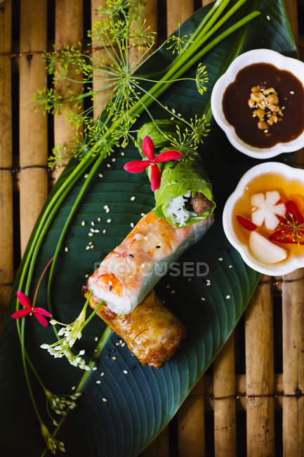 High angle close-up of Vietnamese spring rolls served on banana leaf with sauces. — Stock Photo